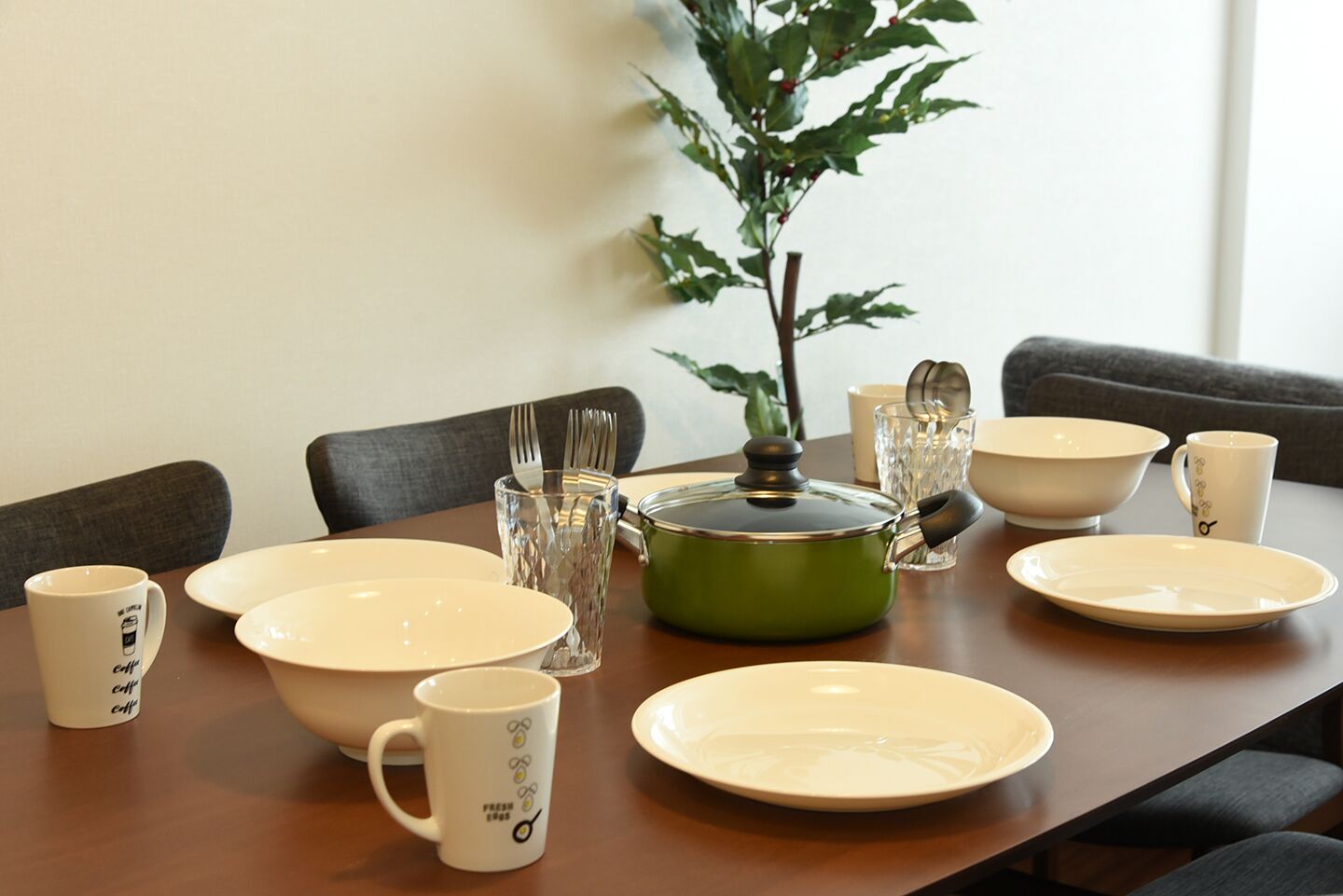 A dining table set with plates, bowls, mugs, and a green pot with a lid.