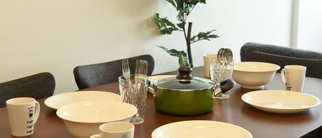A dining table set with plates, bowls, mugs, and a green pot with a lid.