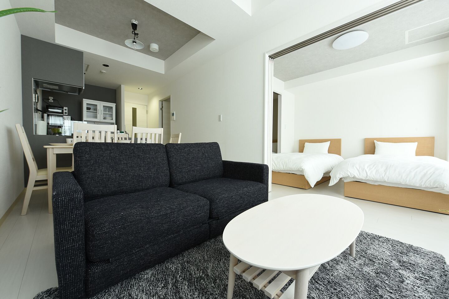 A modern hotel room with a dark grey sofa, a white round table, and a bed with white bedding.