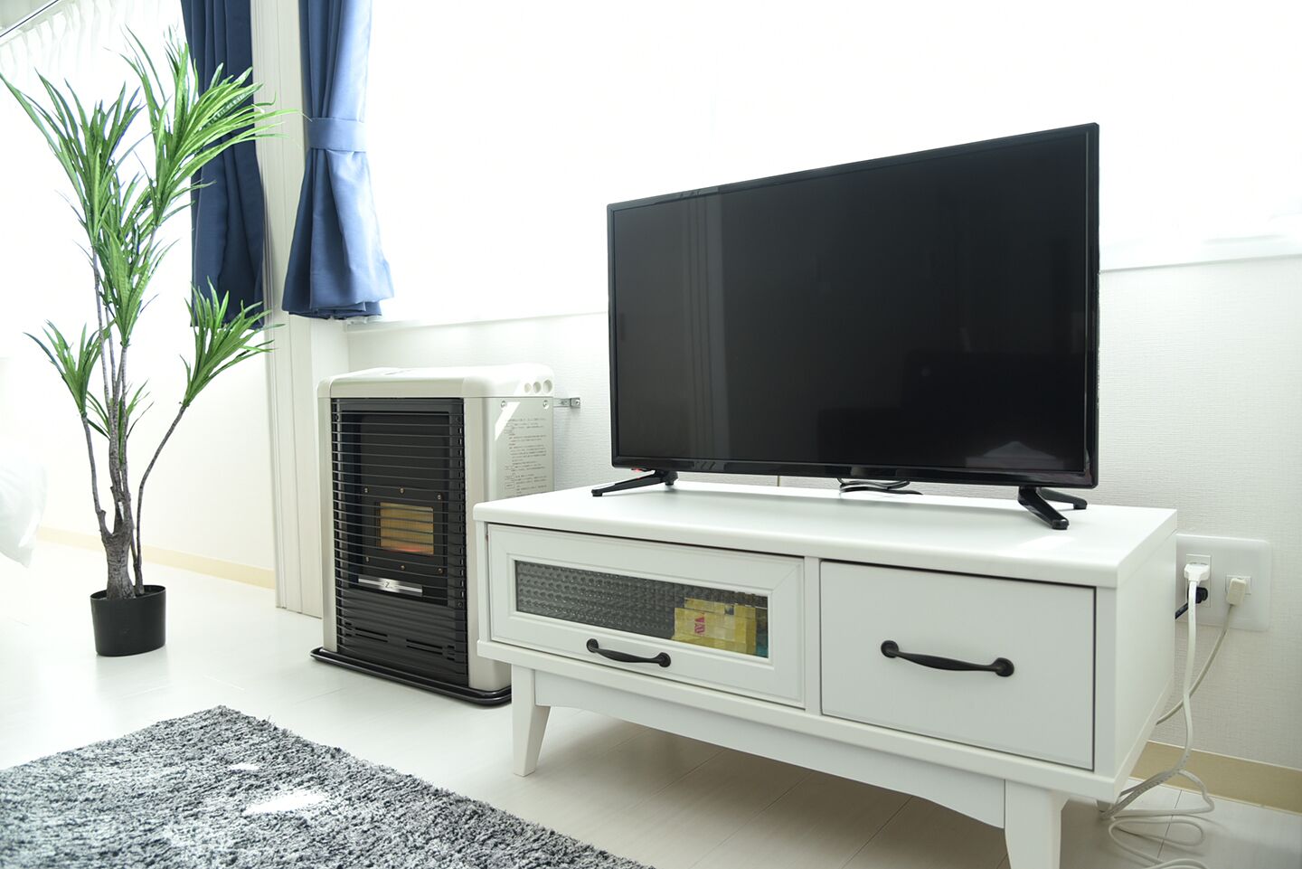 Un mueble blanco para entretenimiento con un televisor de pantalla plana, un aire acondicionado negro y una planta en maceta.
