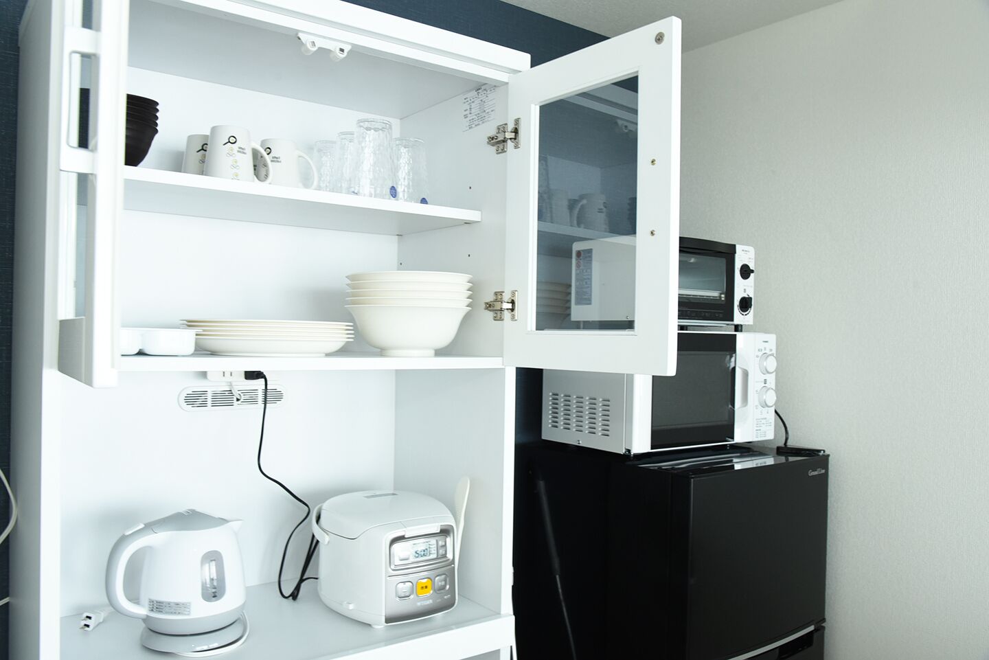 Cozinha equipada com micro-ondas, torradeira, chaleira e prateleiras com louça e copos.