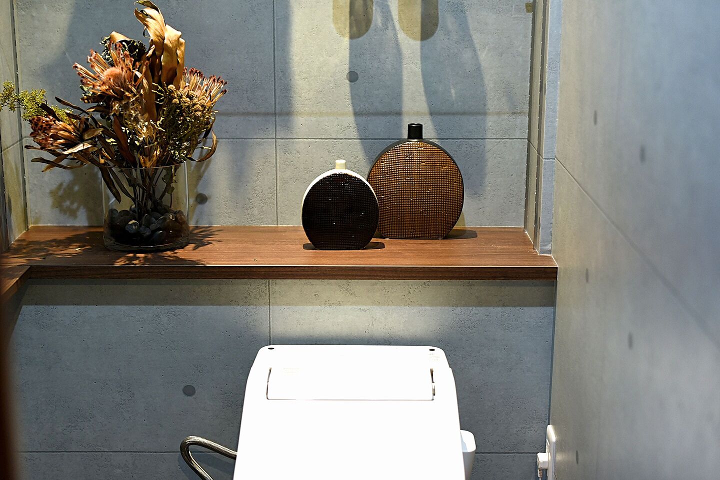 A bathroom with a wooden shelf holding a vase of dried flowers and two speakers.
