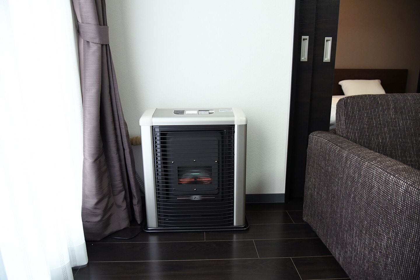 A compact room with a standing heater, a dark sofa, and a curtain.