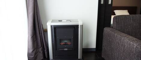 A compact room with a standing heater, a dark sofa, and a curtain.