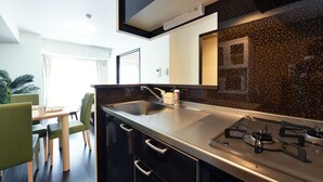 A modern kitchen with a stainless steel countertop, a built-in stove, and a black backsplash. - Sun Court Hongodori Garden Hills (Sapporo)