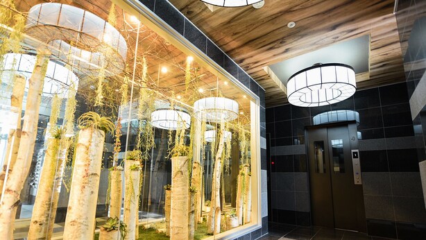 A modern lobby with a glass wall featuring vertical gardens, a checkered floor, and a central elevator. - Sun Court Hongodori Garden Hills (Sapporo)