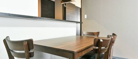 Un comedor con una mesa de madera y cuatro sillas, una ventana pequeña y una puerta.