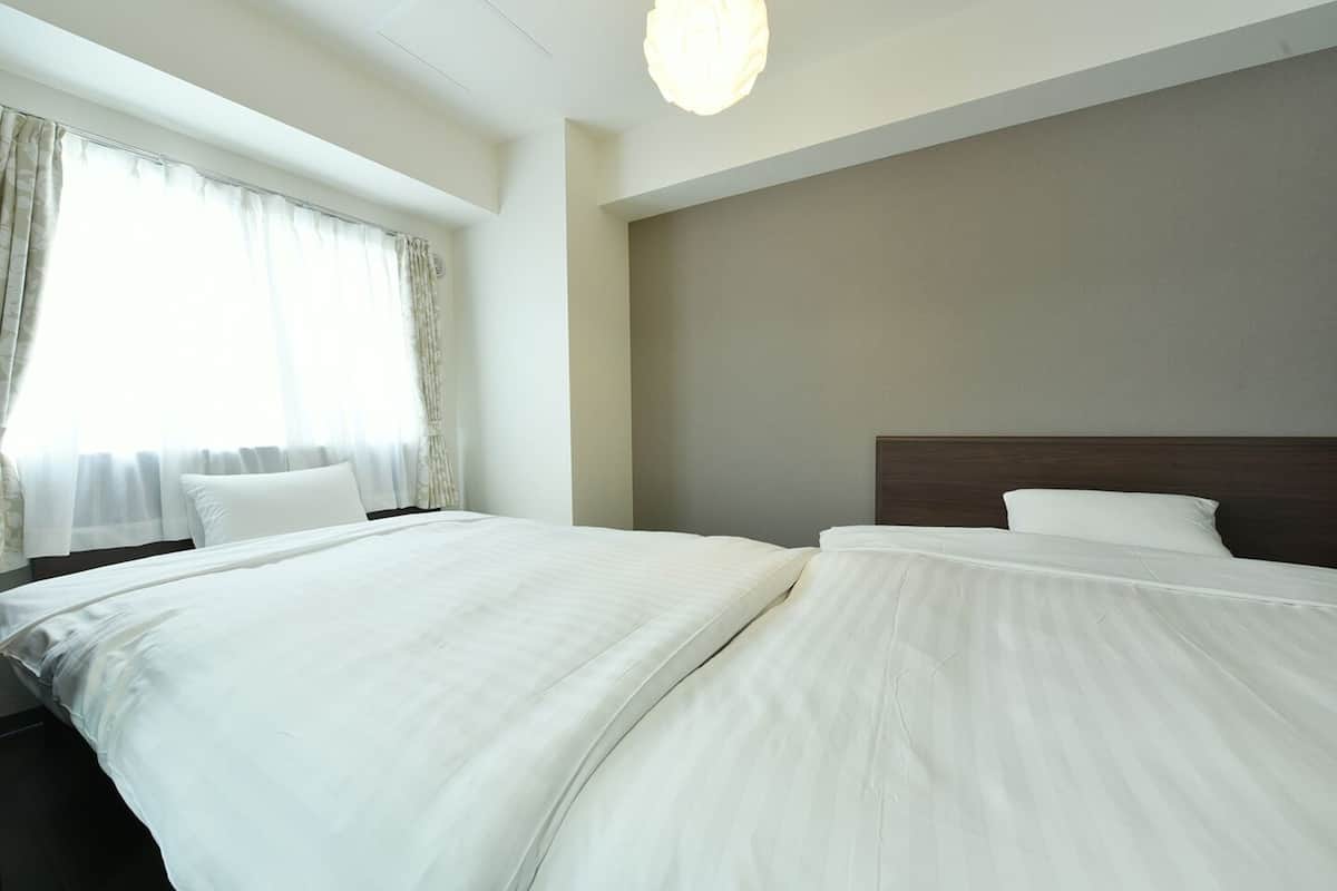 Habitación de hotel con dos camas, un ventanal con cortinas traslúcidas y una lámpara moderna.