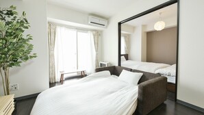 A hotel room with a bed, a mirror, a plant, and a window with curtains. - Sun Court Hongodori Garden Hills (Sapporo)