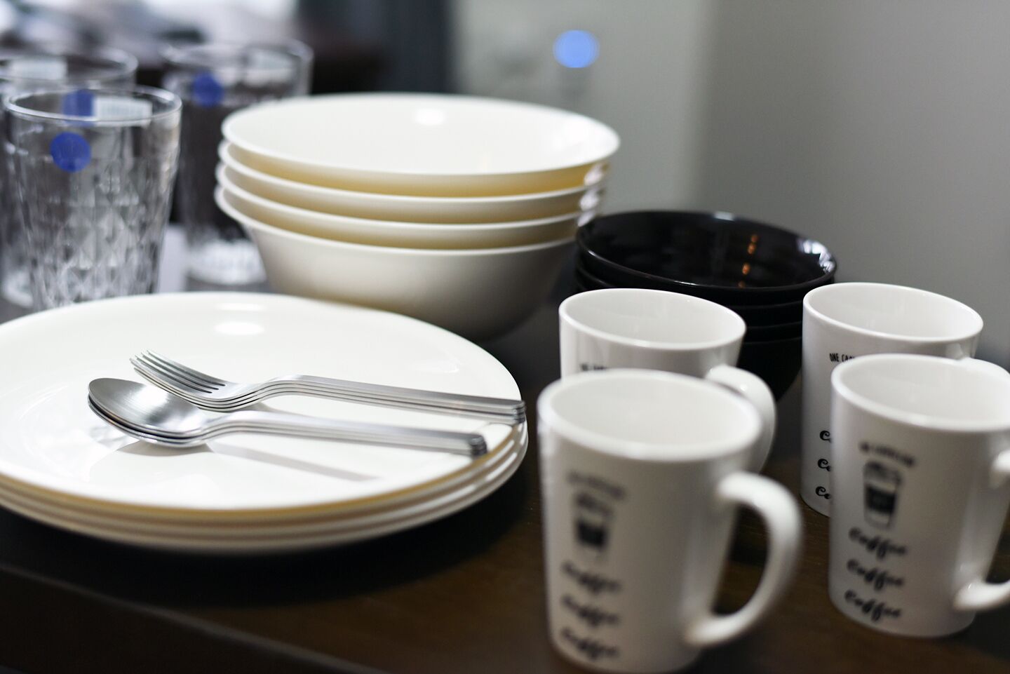 A dining table with stacked plates, a fork, and white mugs with text.