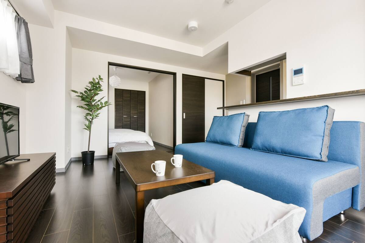Ein modernes Hotelzimmer mit einem blauen Sofa, einem Holztisch, einem weißen Bett und einem Blumentopf.