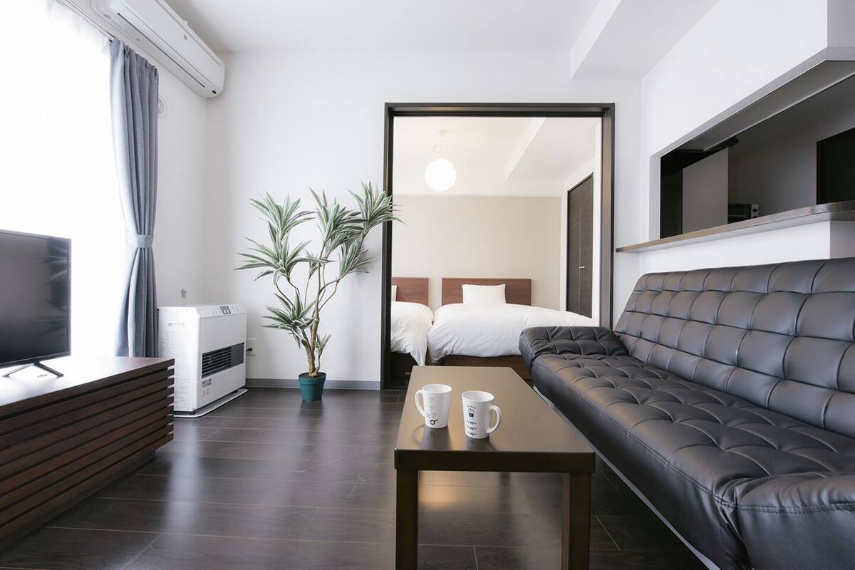Ein modernes Hotelzimmer mit einer Couch, einem Fernseher, einem Couchtisch, einer Topfpflanze und einem Bett.