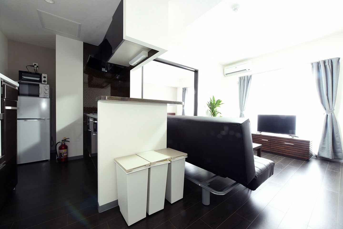 Um espaço de estar moderno com cozinha, um sofá de couro preto, uma mesa pequena e uma TV.