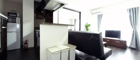 Um espaço de estar moderno com cozinha, um sofá de couro preto, uma mesa pequena e uma TV.