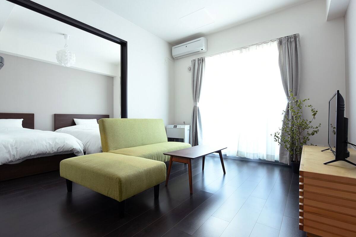 Ein Hotelzimmer mit einem Bett, einem grünen Sessel, einem kleinen Tisch, einem Fernseher und einer Pflanze.
