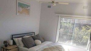 Ein Hauptschlafzimmer mit Bett, Nachttisch und einem Fenster mit Blick auf Bäume.