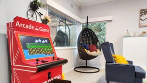 Ein Zimmer mit einem roten Arcade-Spiel, einem blauen Stuhl, einem Hängestuhl und einem kleinen schwarzen Hocker.