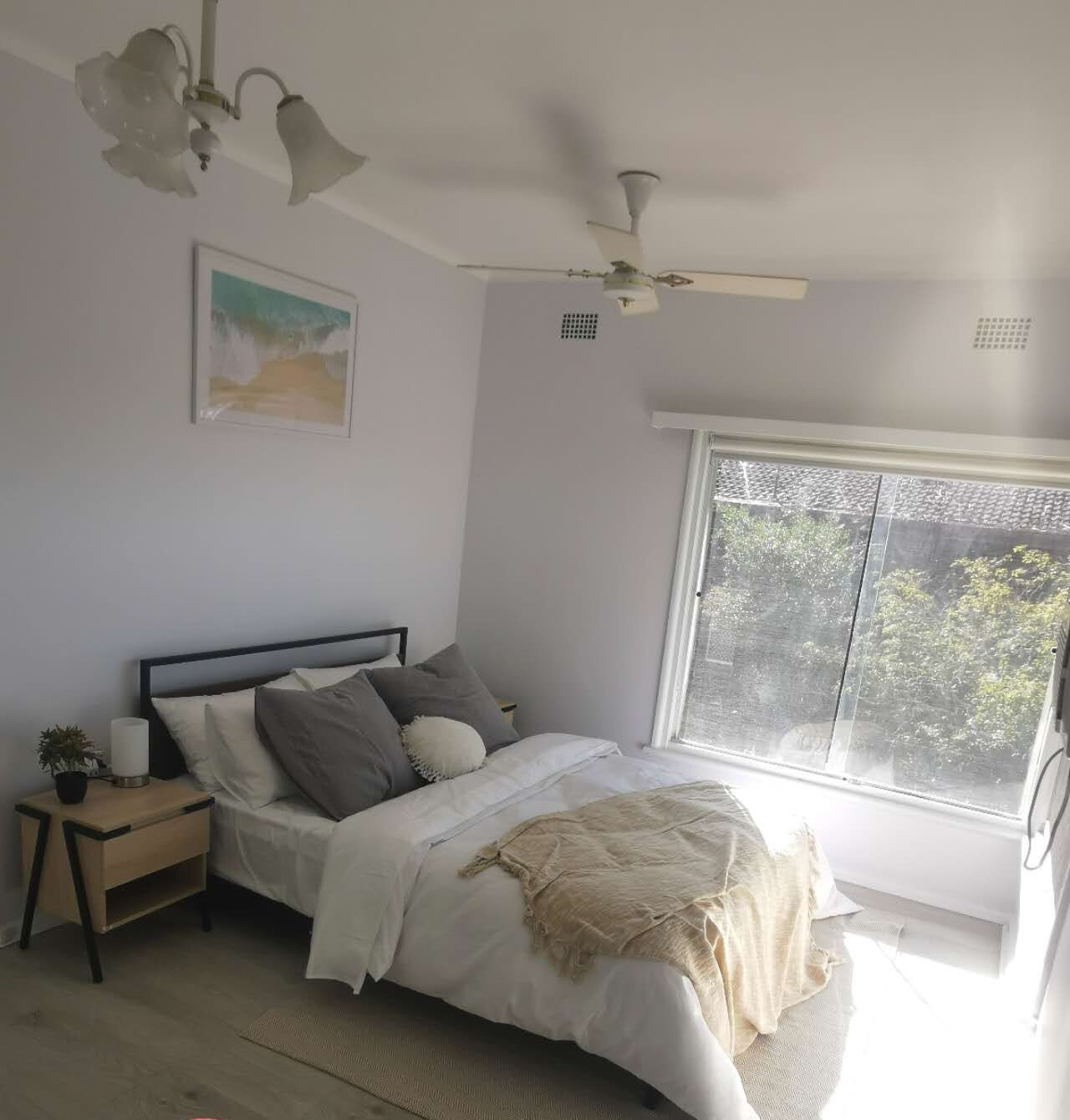 A main bedroom with a bed, nightstand, and a window with a view of trees.