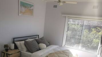 A main bedroom with a bed, nightstand, and a window with a view of trees.