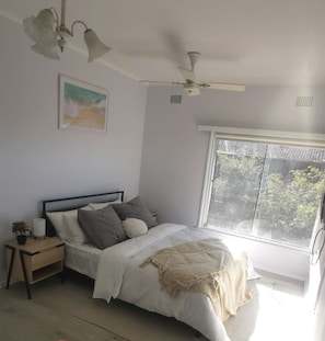 A main bedroom with a bed, nightstand, and a window with a view of trees. - Lakeview house in Gosford CBD (Gosford)