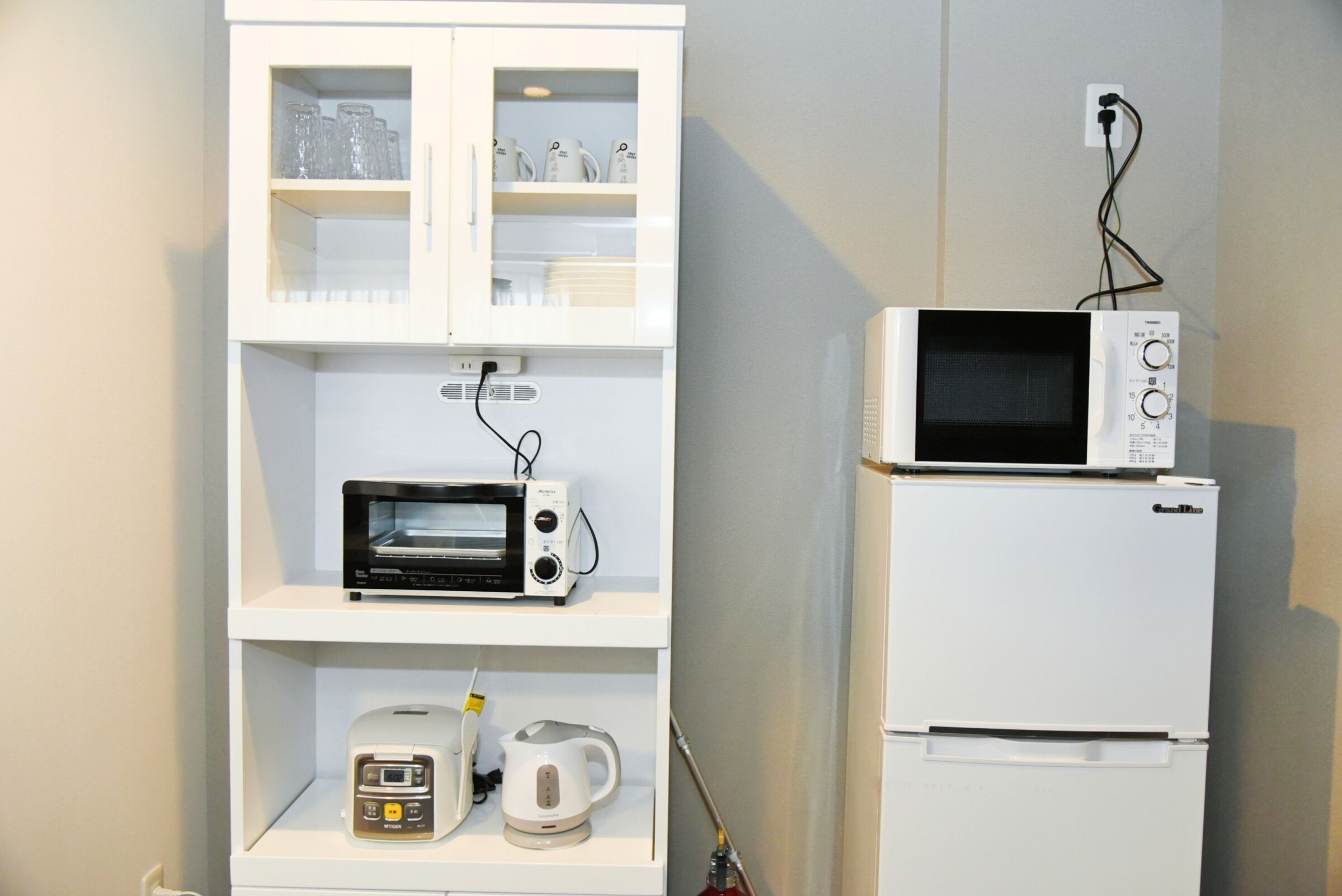 A kitchenette with a microwave, toaster, and coffee maker on shelves, and a refrigerator below.