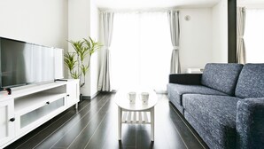 Een moderne woonkamer met een flatscreen televisie, een grijze bank, een witte salontafel en een potplant.