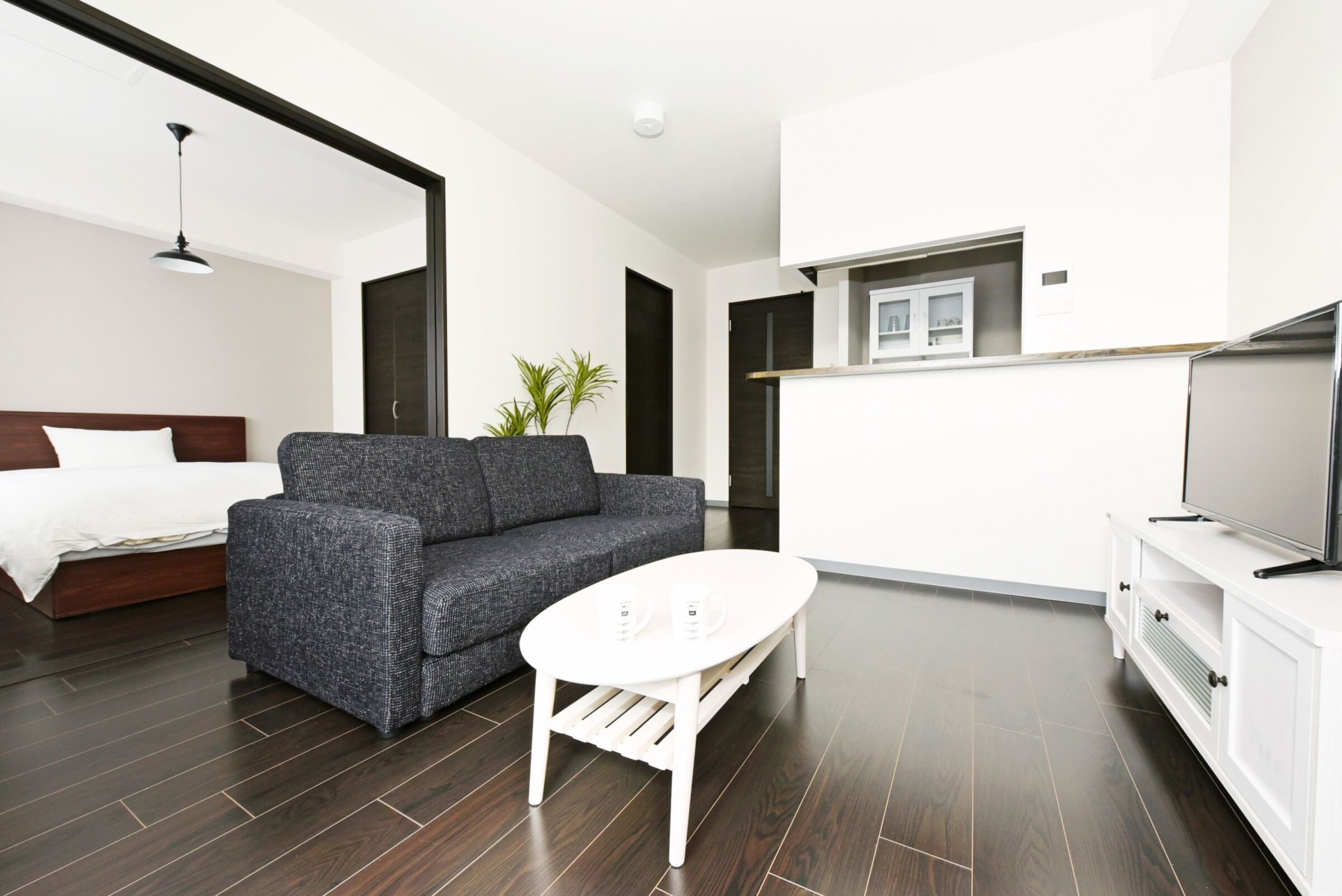 A modern living room with a sofa, a coffee table, a TV, and a bed.
