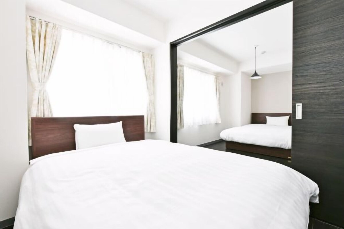 Moderni hotellihuone, jossa on suuri sänky, tumma puinen pääty ja suuri peili, joka heijastaa huonetta.