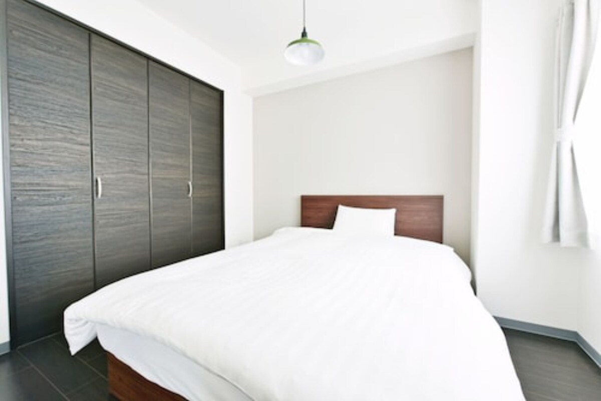 Een moderne slaapkamer met een groot bed, een houten hoofdeinde en een donkerhouten garderobe.