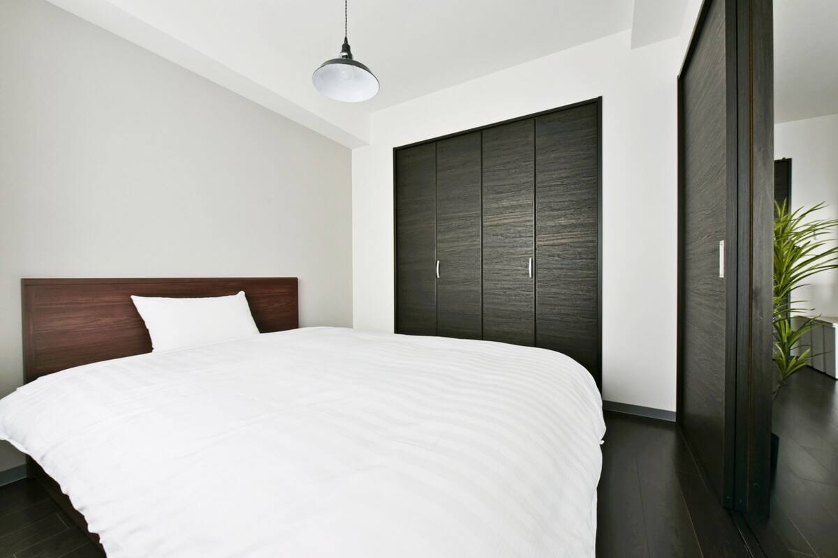 Ein modernes Schlafzimmer mit einem großen Bett, einem dunklen Holzschrank und einer Pendelleuchte.