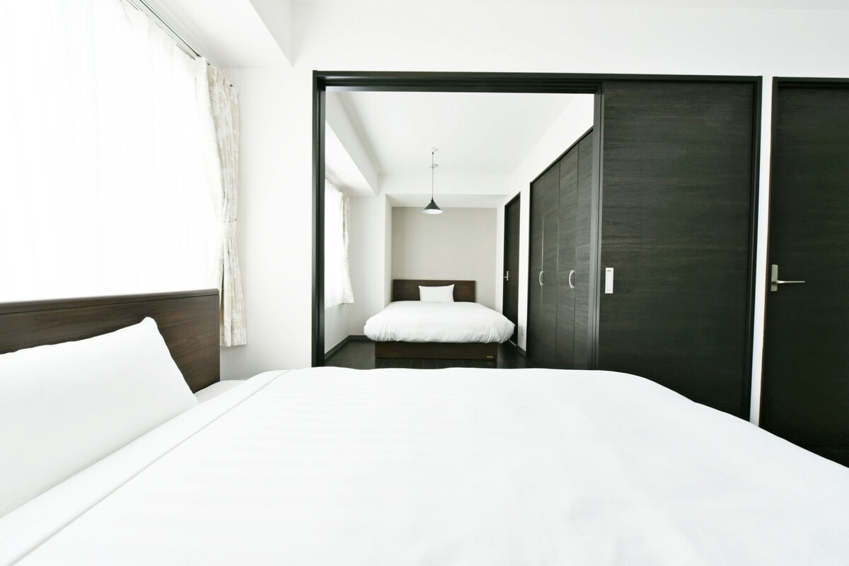 Een moderne hotelkamer met een groot bed, een donkere kledingkast en uitzicht op een gang.