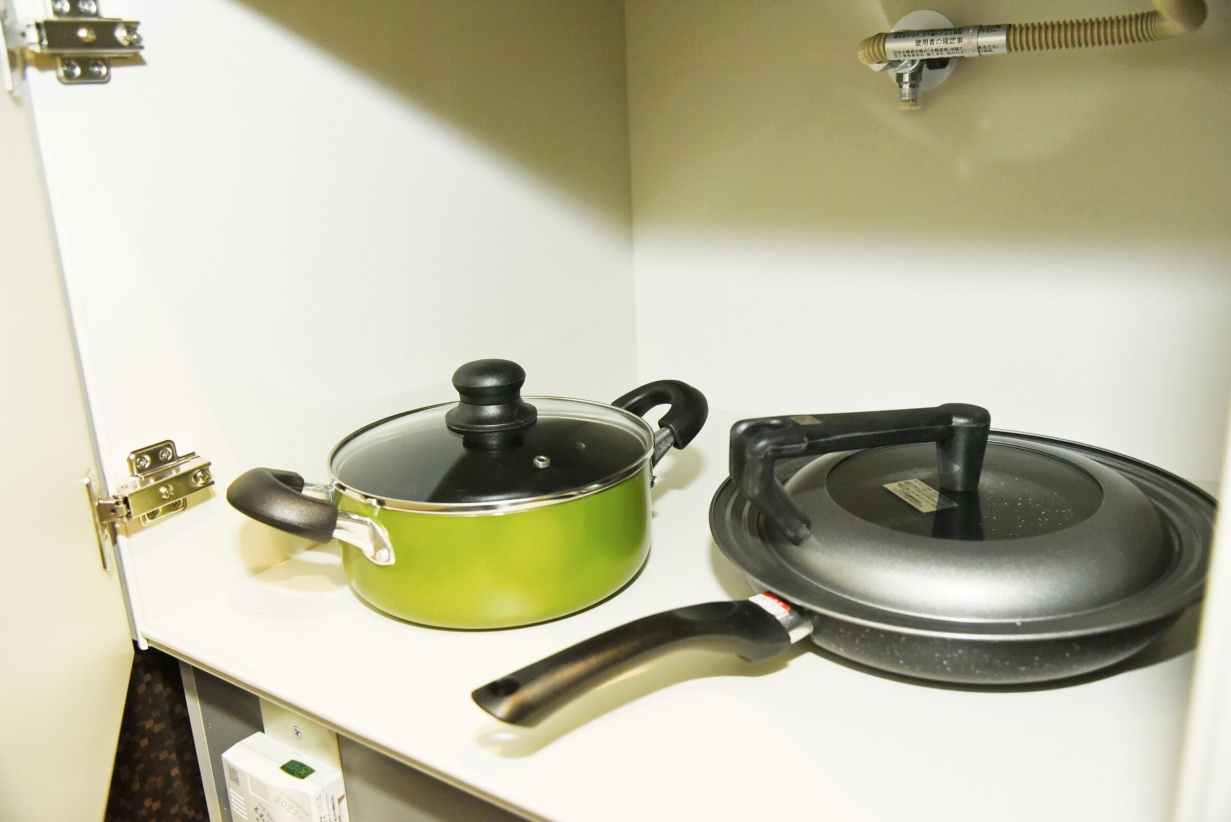 Uma cozinha com bancada branca, uma panela verde com tampa preta e uma frigideira preta com tampa.
