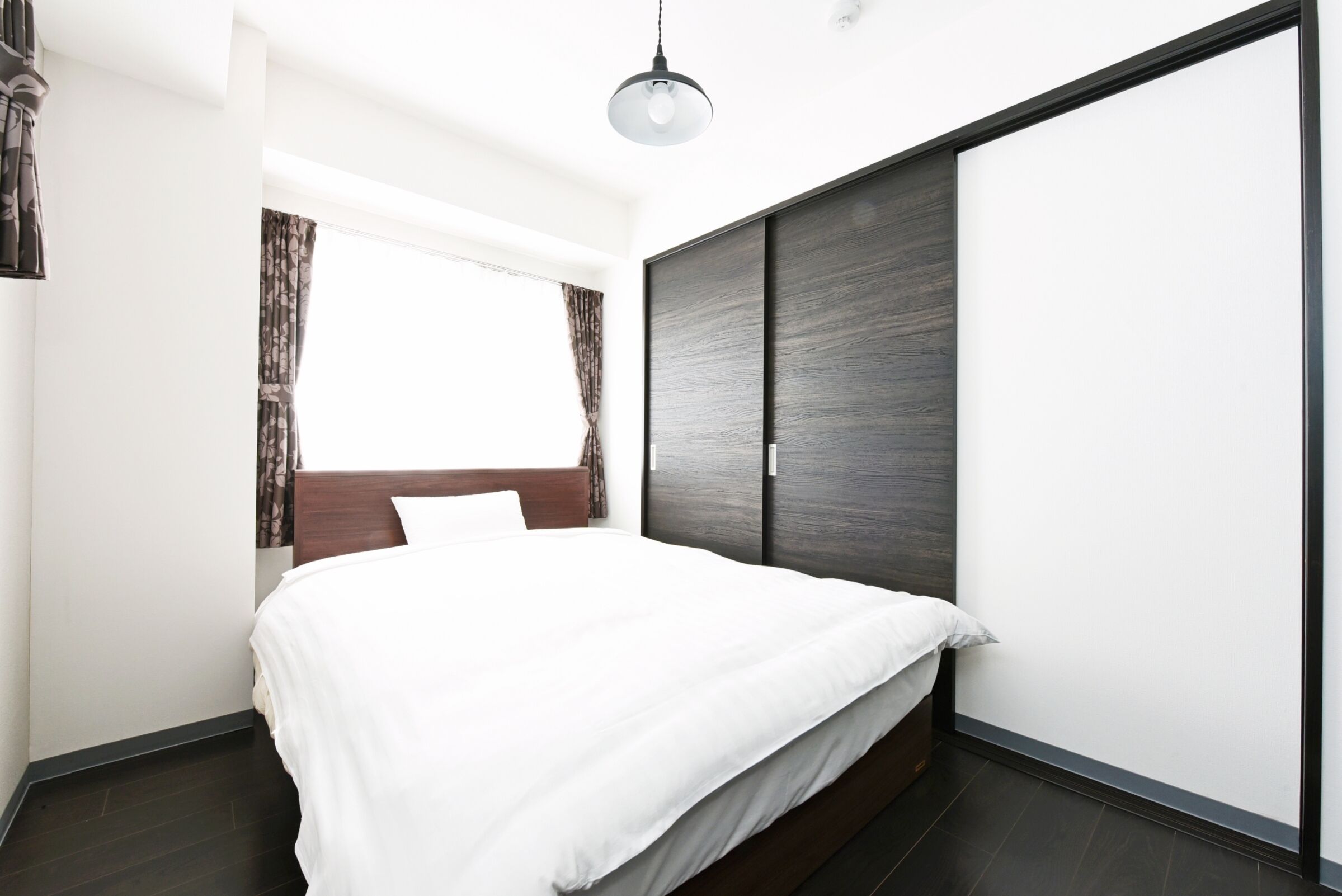 Quarto moderno com cama grande, guarda-roupa de madeira escura e janela com cortinas.
