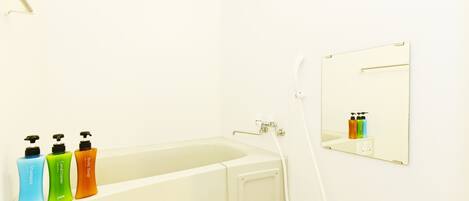 Une salle de bain avec une baignoire, une douche et un miroir. Trois bouteilles de shampoing, d’après-shampoing et de gel douche sont posées sur le bord de la baignoire.