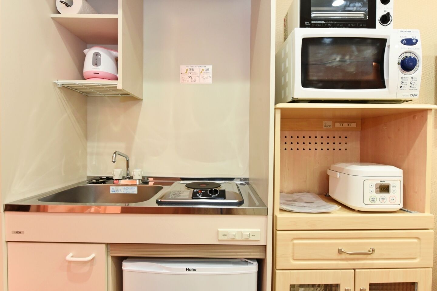 A compact kitchenette with a sink, stove, microwave, and a rice cooker.