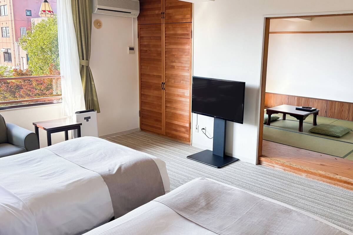 A hotel room with two beds, a TV, a small table, and a view of a traditional Japanese room.