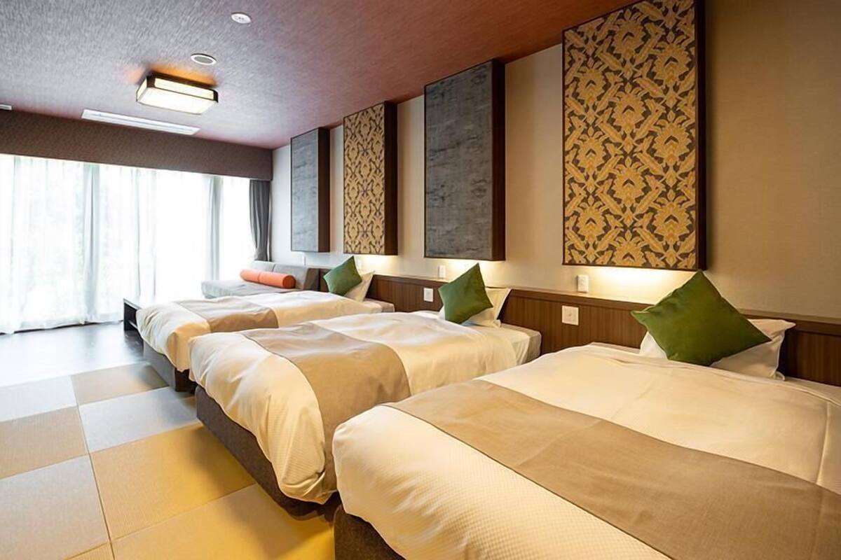 A hotel room with three beds, a large window, and decorative wall panels.