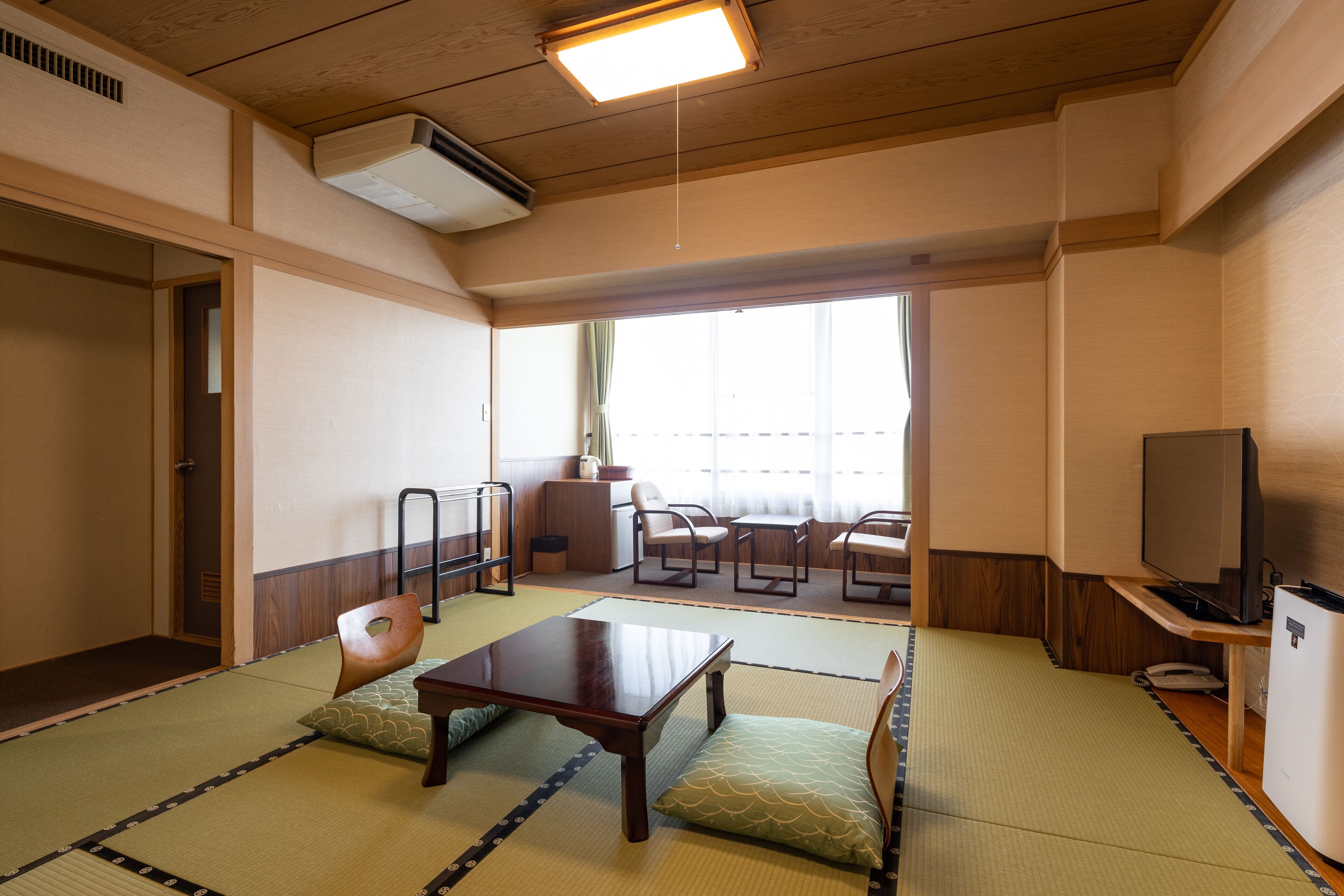 Une pièce de style japonais traditionnel, avec un sol recouvert de tatamis, une table basse, des chaises, un téléviseur et une porte coulissante.