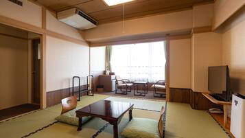 A traditional Japanese room with tatami flooring, a low table, chairs, a television, and a sliding door.