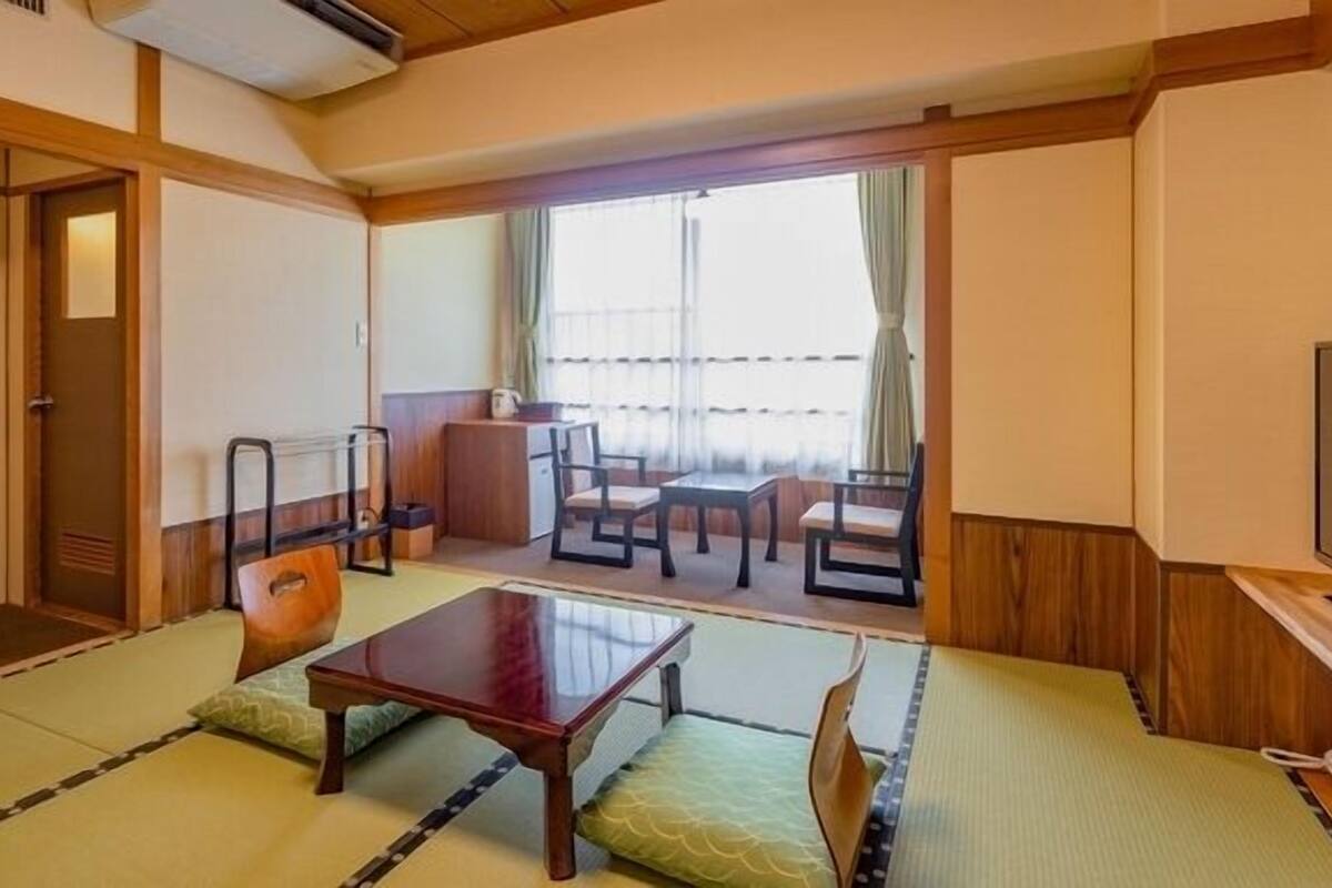 A traditional Japanese-style room with tatami flooring, a low wooden table, and a TV on the right.