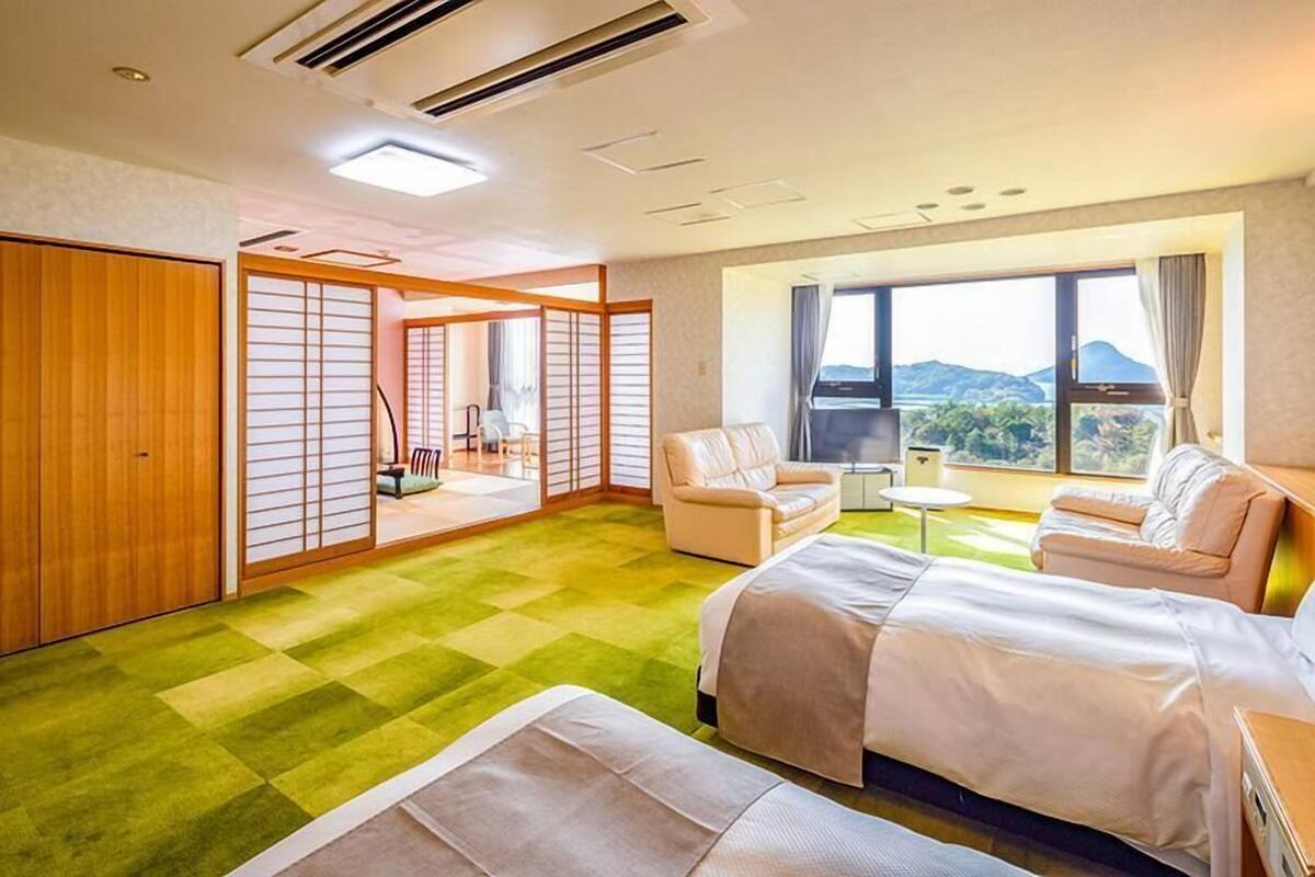 A hotel room with a large bed, two armchairs, a small table, and a view of the outdoors.