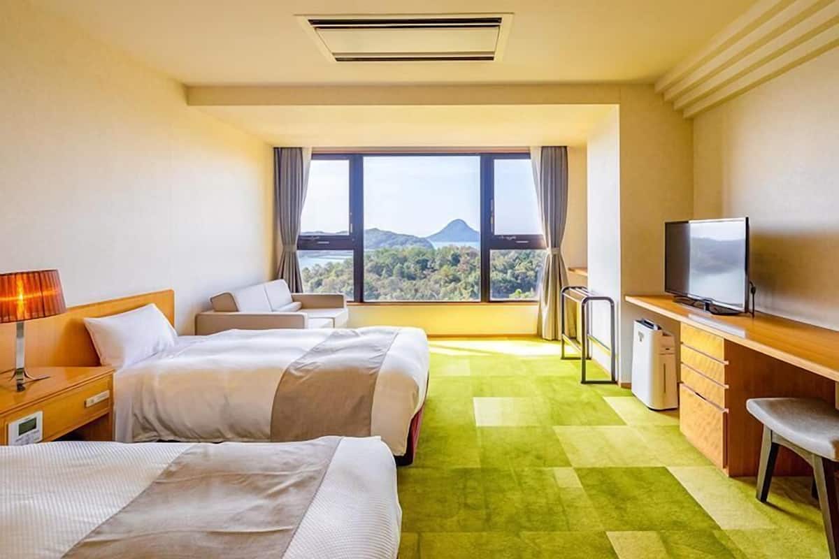 A hotel room with two beds, a desk, a television, and a view of the outdoors.