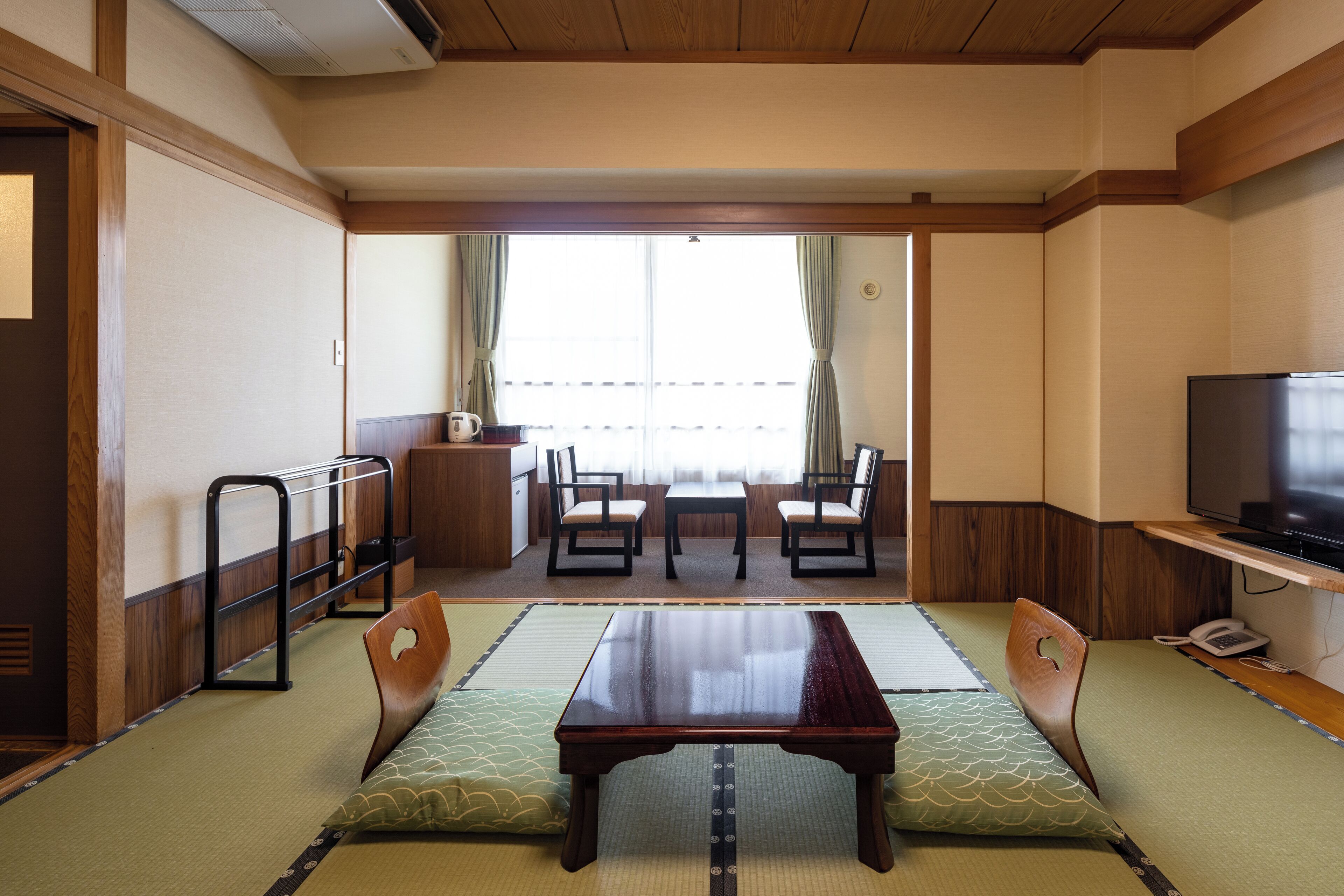 Una habitación tradicional japonesa con suelo de tatami, una mesa baja y un televisor sobre un soporte de madera.