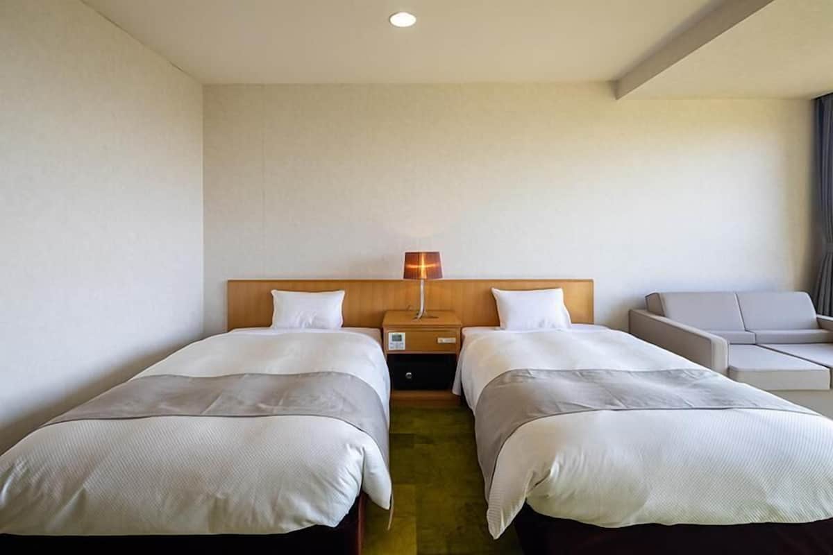 A hotel room with two beds, a nightstand with a lamp, a sofa, and a small table.