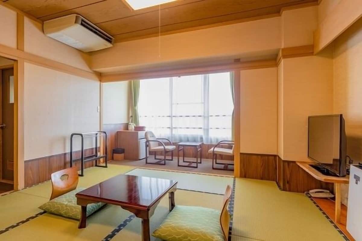 A traditional Japanese room with tatami flooring, a low table, chairs, a television, and a sliding door leading to a balcony.