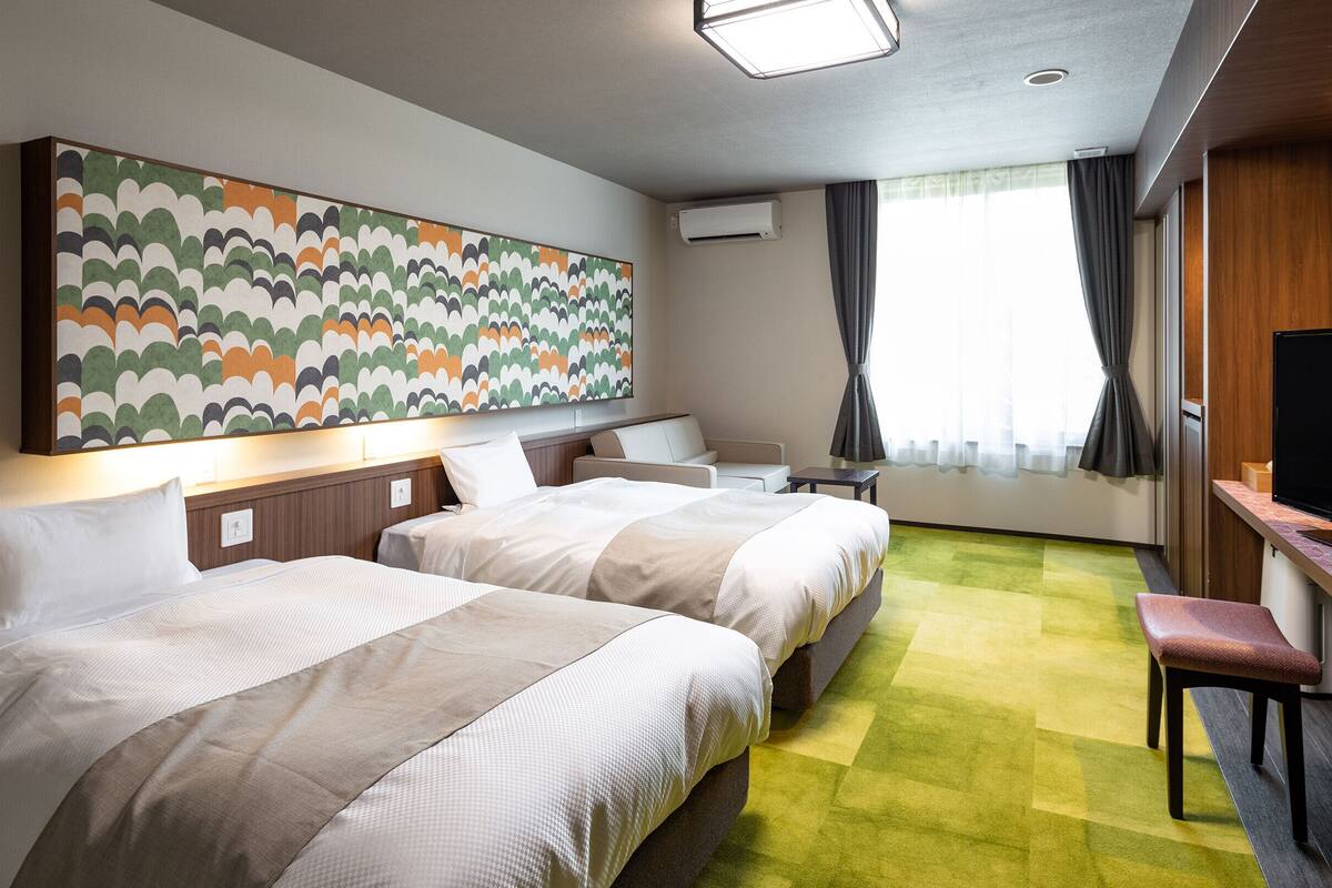 A hotel room with two beds, a TV, a desk, and a large abstract painting on the wall.