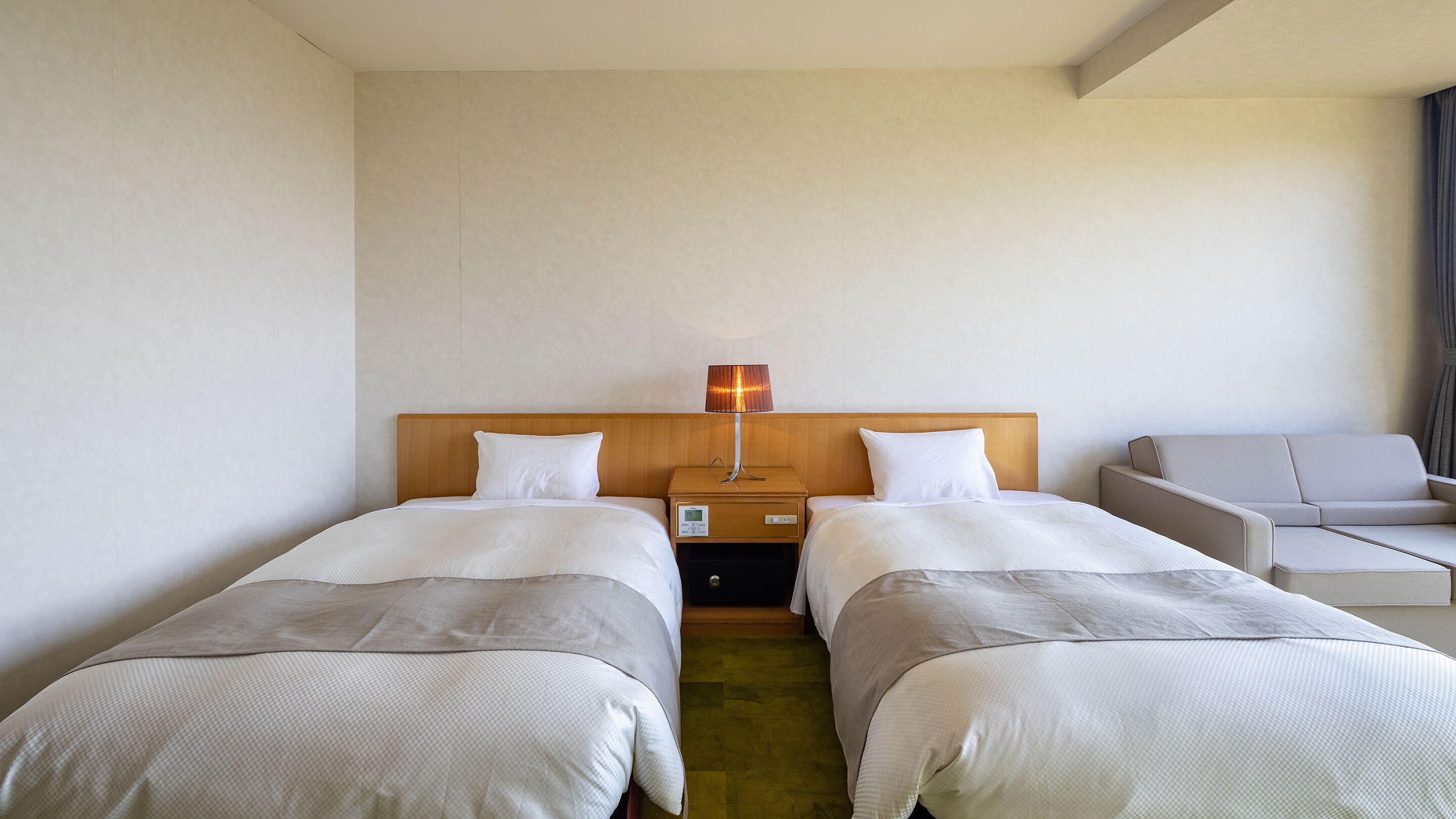 Ein Hotelzimmer mit zwei Betten, einem Nachttisch mit Lampe, einem kleinen Tisch und einem Sofa.
