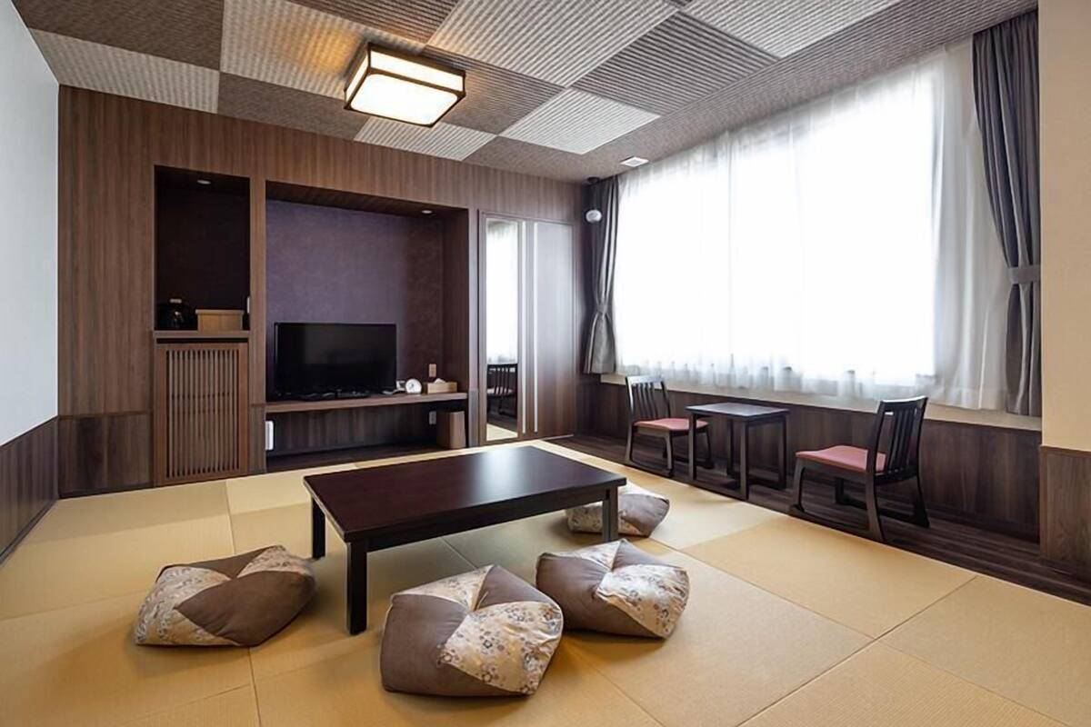 A modern living room with tatami flooring, a large dark table, and a flat-screen TV.