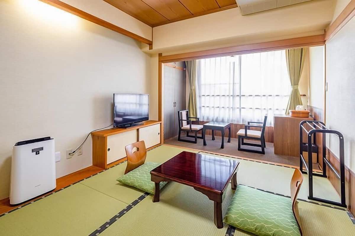 A traditional Japanese room with tatami flooring, a low wooden table, a television, and a sliding door leading to a balcony.