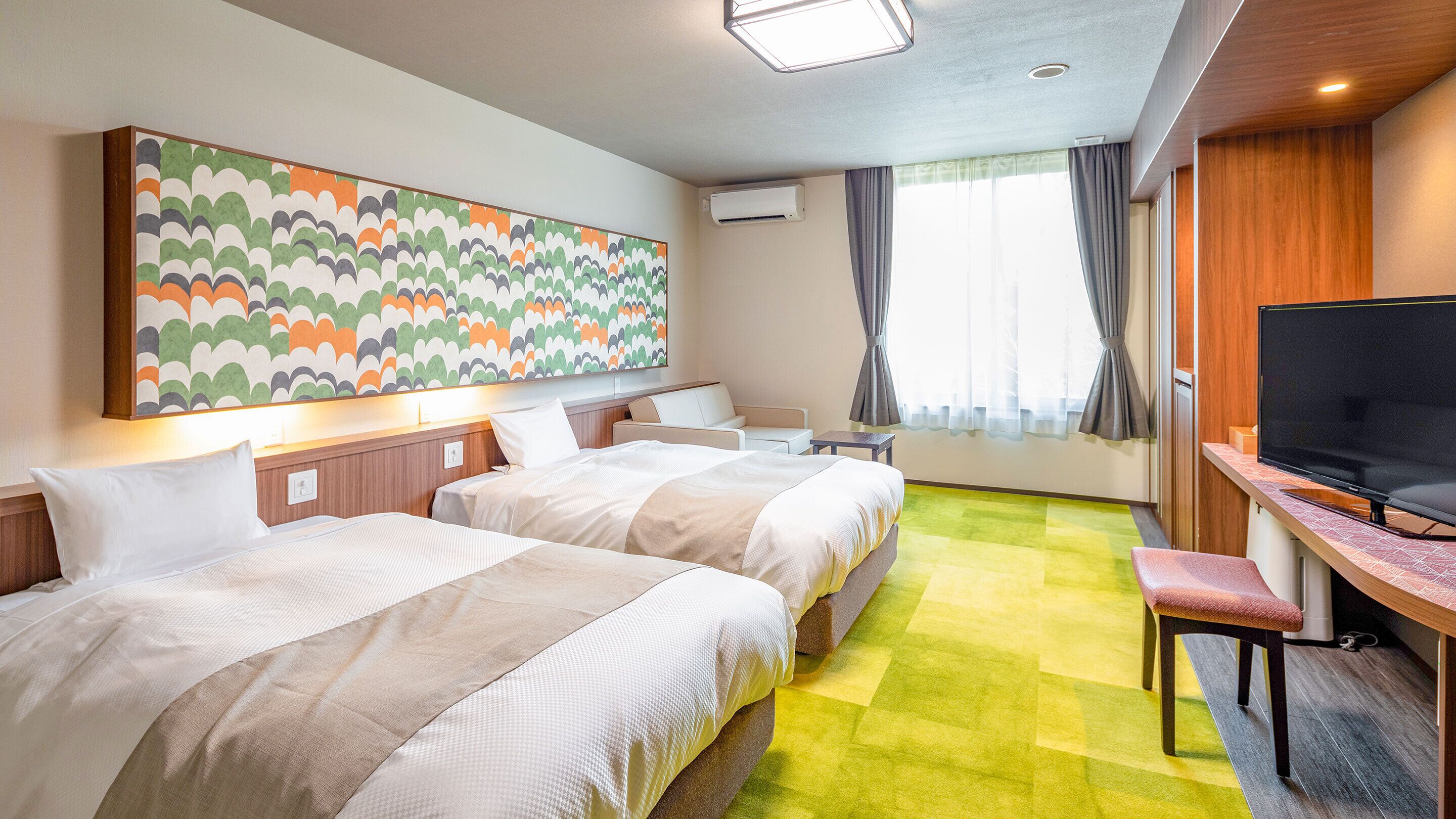 Ein Hotelzimmer mit zwei Betten, einem Fernseher, einem Schreibtisch, einem Stuhl, einem großen, farbenfrohen Kunstwerk und einem Fenster mit Vorhängen.